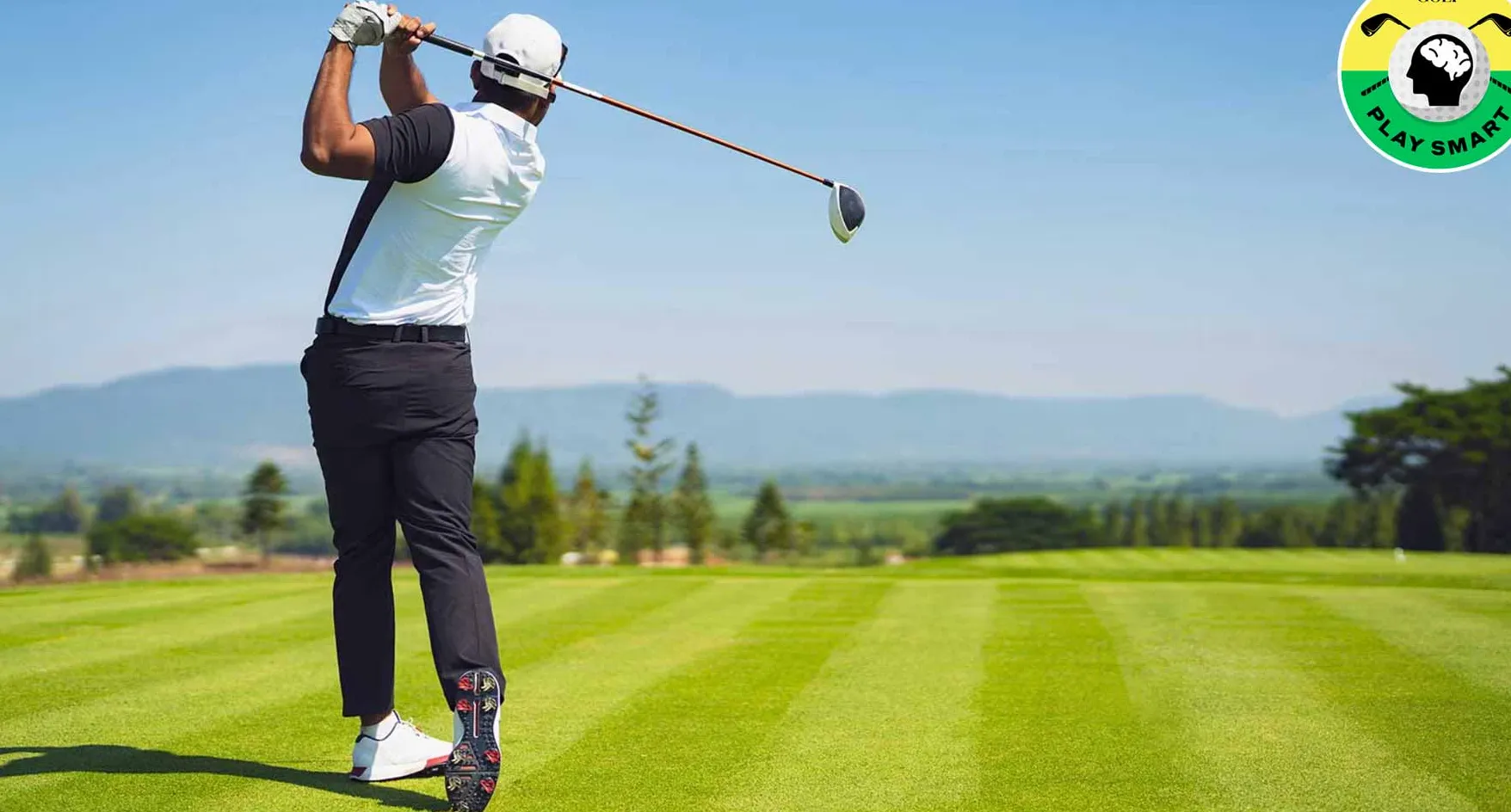 golfer in black pants and white shirt swings golf club on golf course with ocean in the distance