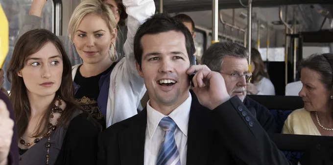 A man in a suit taking a call in a bus surrounded by other people