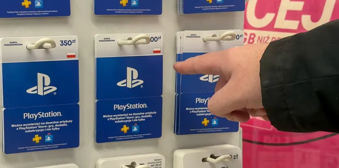 Person pointing at PlayStation physical gift cards on a store rack.