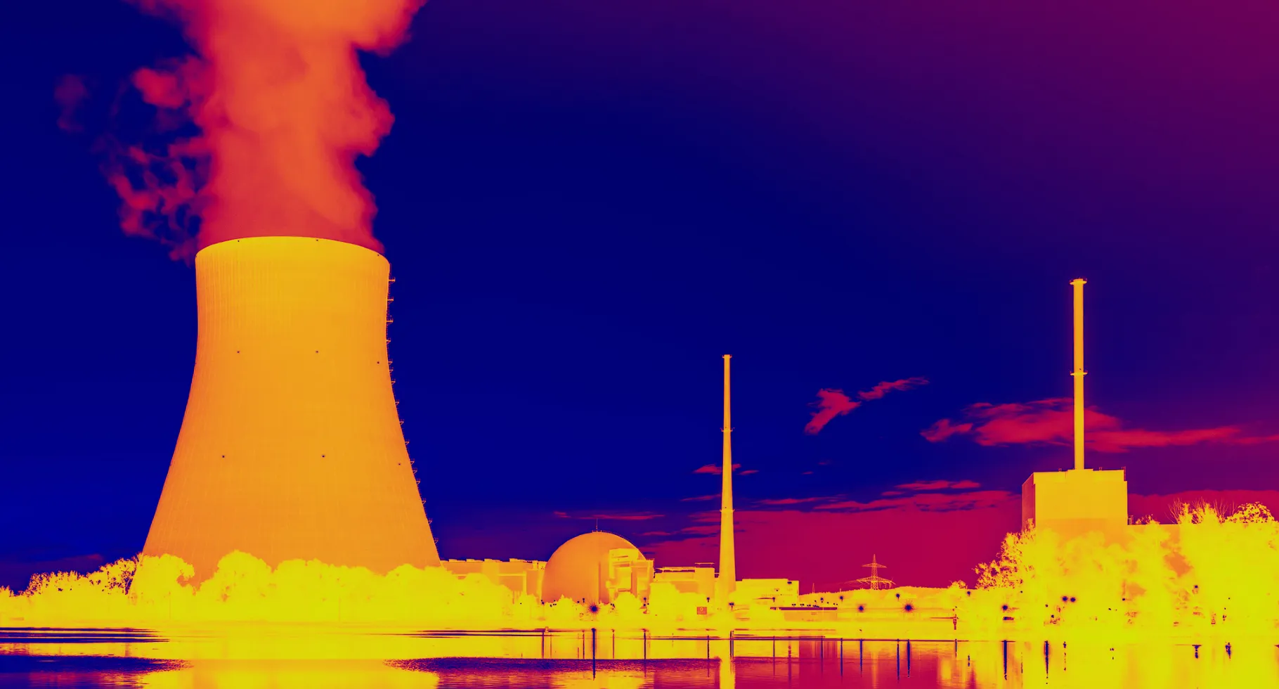 This infrared image shows a glowing orange nuclear power plant releasing hot yellow smoke near various outbuildings with blue water and sky above and below