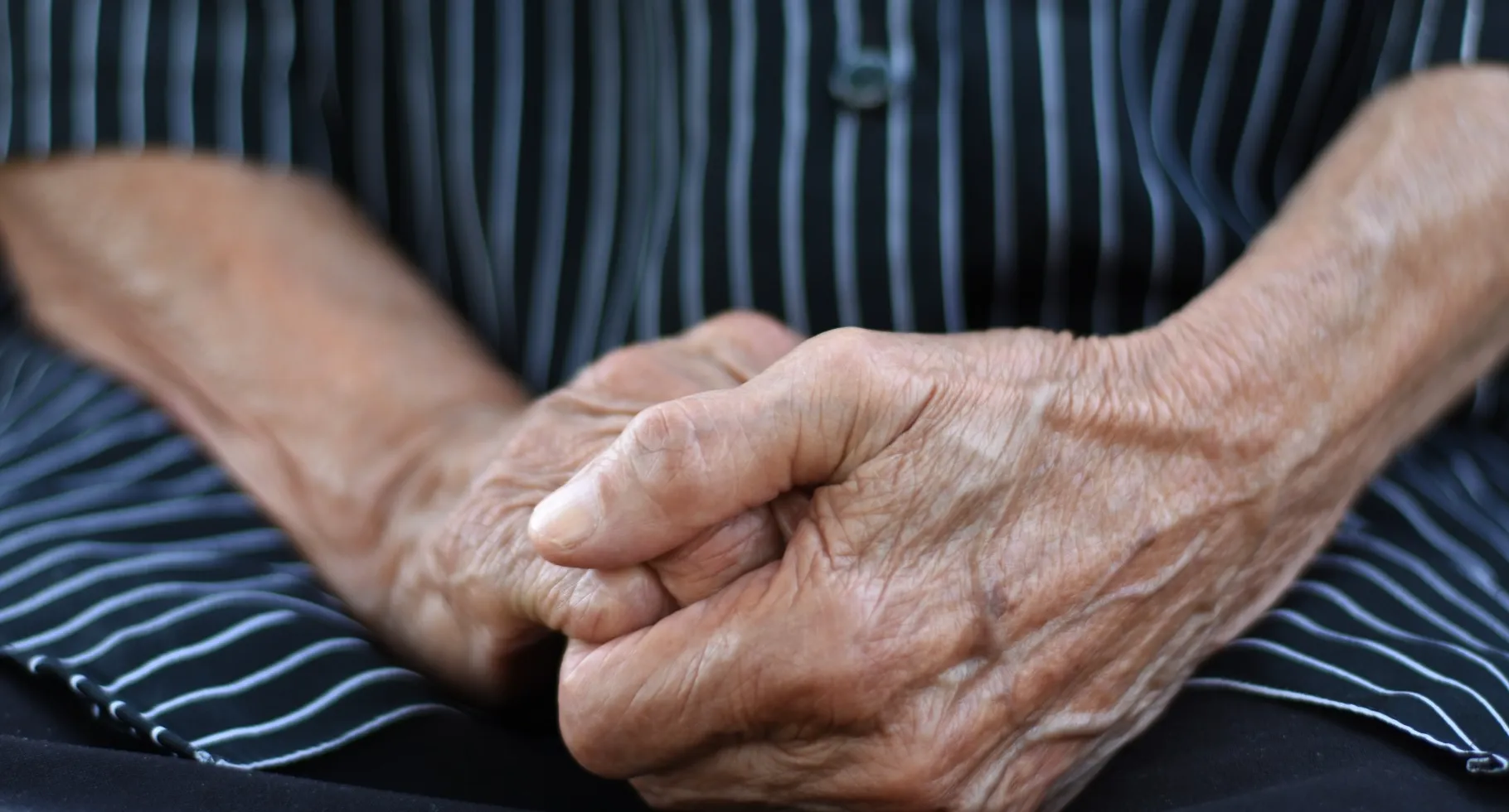 Close-up of the hands of an elderly person that are crossed together over their lap.