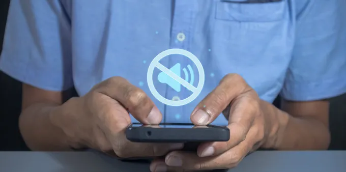 Man holding phone with mute sound symbol.