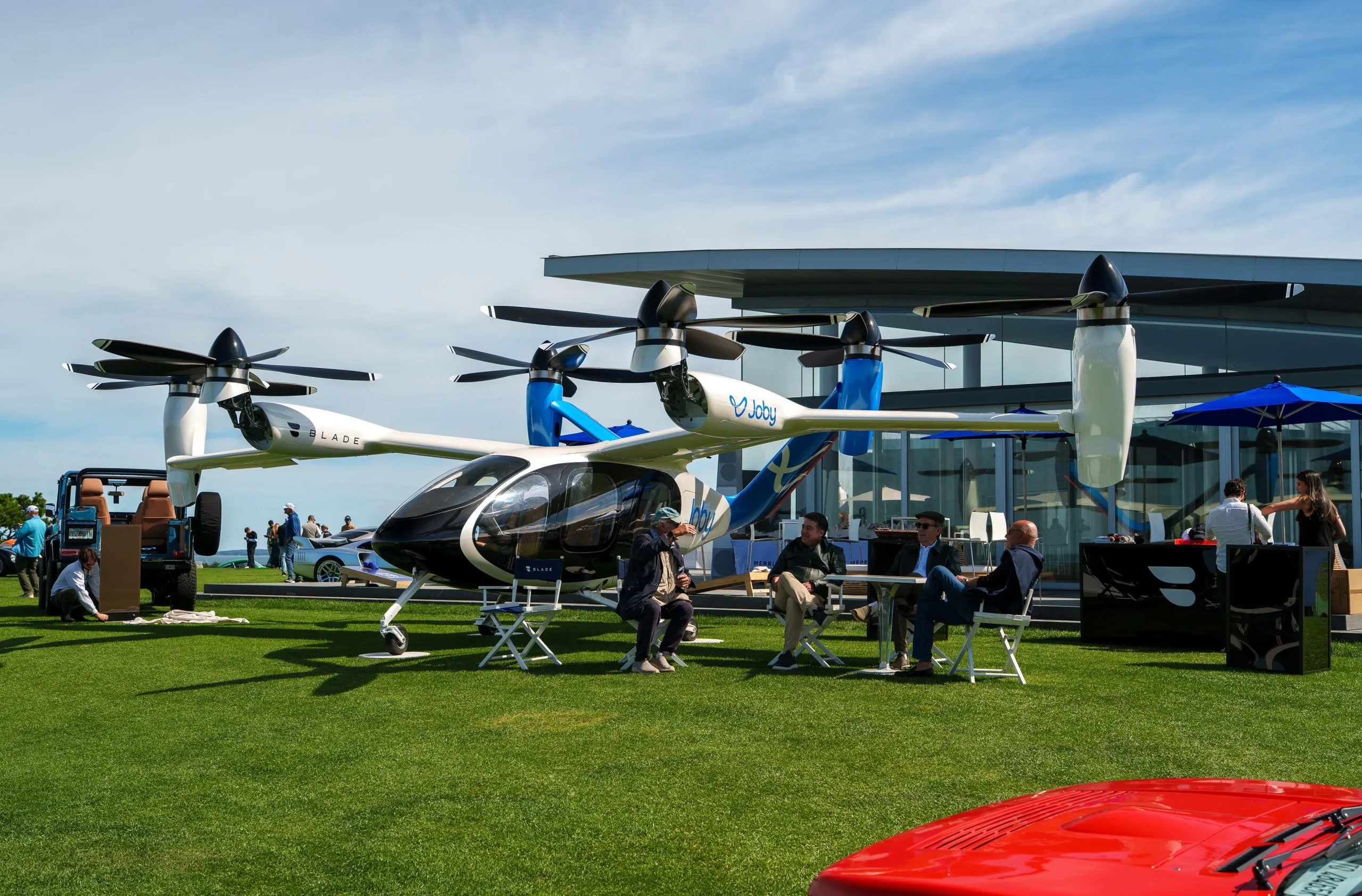 A futuristic eVTOL aircraft showcased on a sunny day, with people interacting and seated nearby.