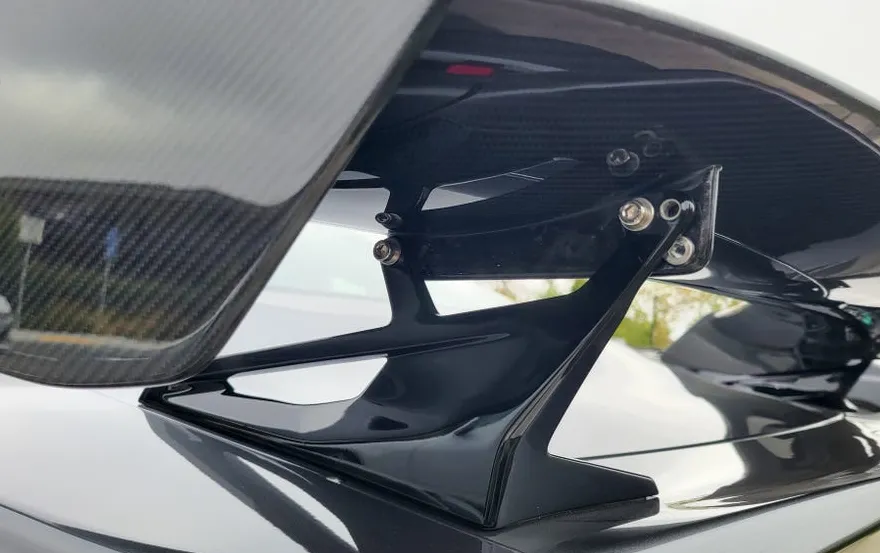 A close-up of a carbon fiber car spoiler mounted on a vehicle.