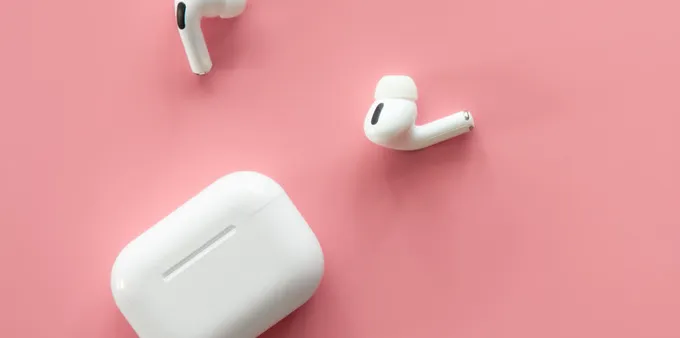 A pair of white earbuds and their case lay on a pink surface.