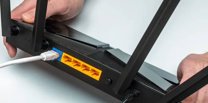 Person showing the rear of a router with cables connected.